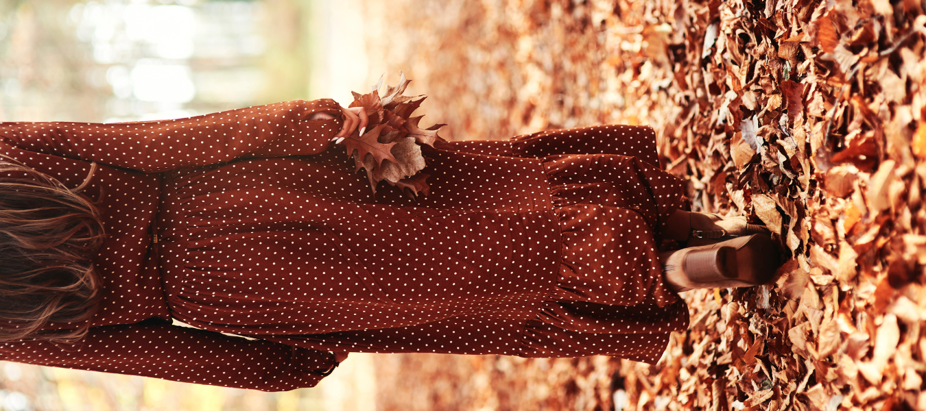Jesienna stylizacja – sukienka w grochy w kolorze bordo i brązowe botki damskie na obcasie w parku pełnym liści