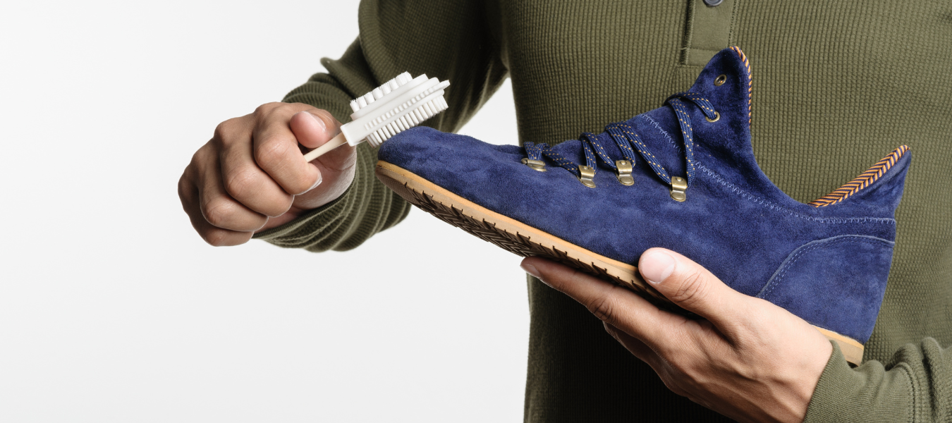Czyszczenie butów zamszowych – mężczyzna szczotkuje niebieskie buty zamszowe specjalną szczotką do zamszu i nubuku