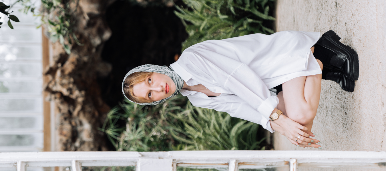 Stylowa kobieta w białej koszuli oversize, z apaszką na głowie i czarnymi skórzanymi botkami – jesienna moda damska 2025