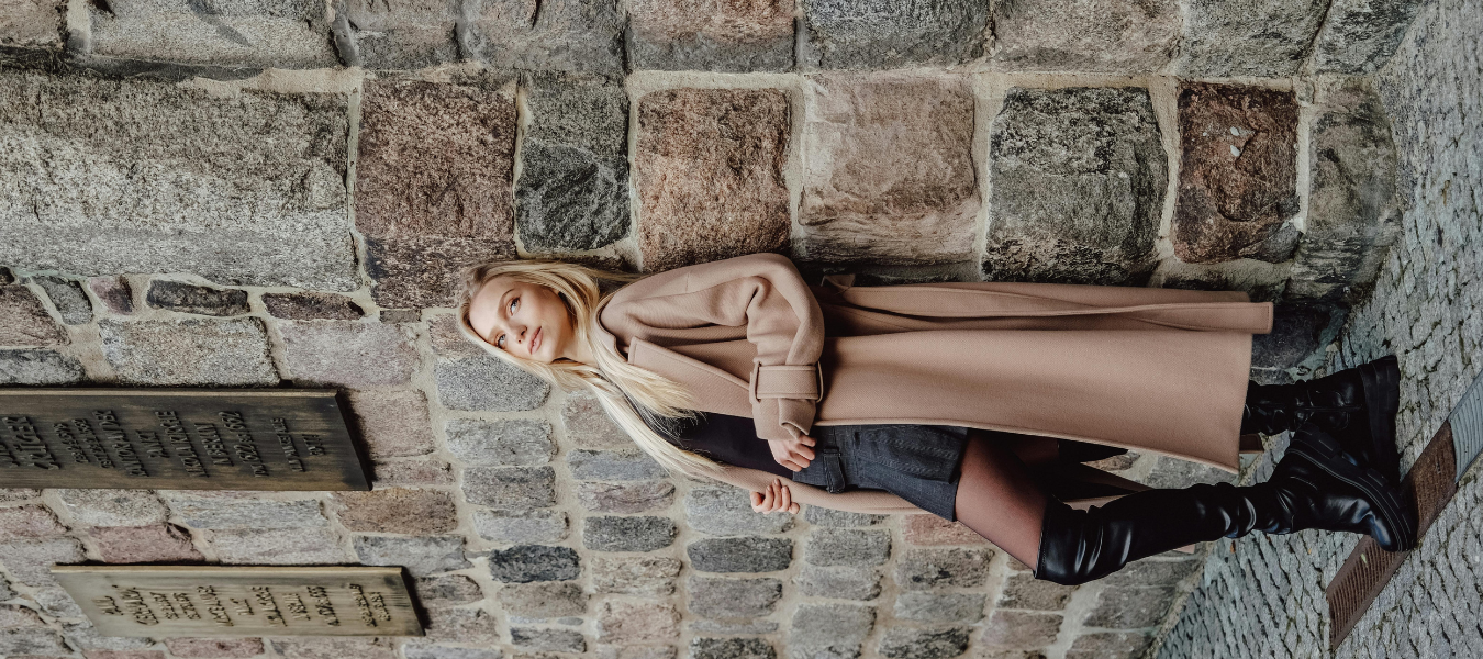 Stylowa kobieta w długim beżowym płaszczu, czarnych kozakach over the knee i krótkiej sukience – jesienna elegancka stylizacja 2025
