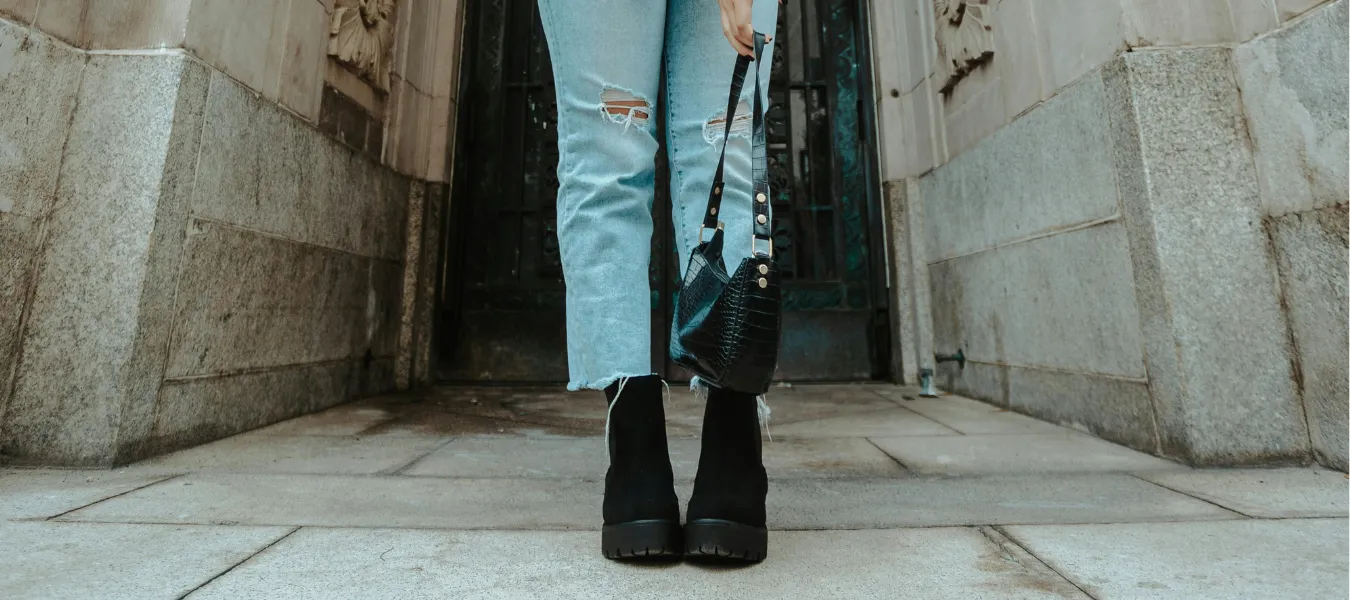 Czarne botki zestawione z dziurawymi jeansami i czarną torebką